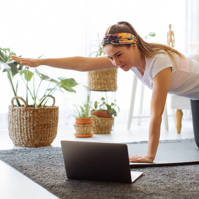 Woman in her home stretching while speaking to doctor on computer through telerehabilitation